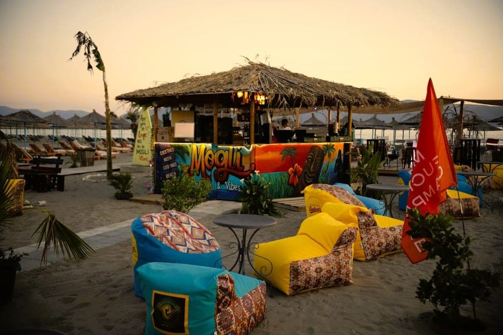 Mogli Lounge beach bar at sunset — colorful bean bags, thatched bar, and sea in the background
